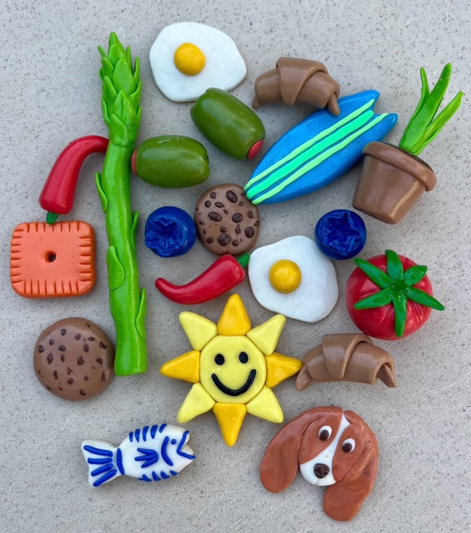 Colorful handmade clay magnets shaped like food, a fish, a sun, and a basset hound